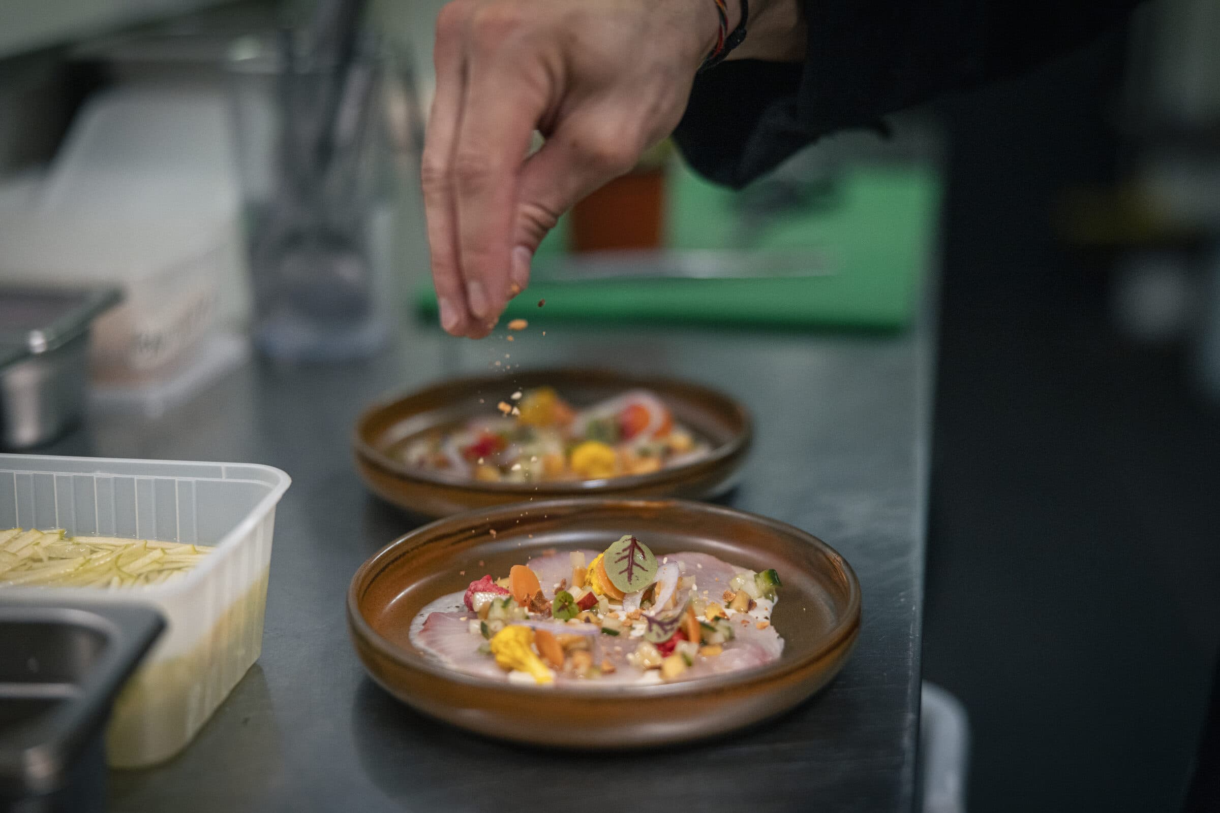 Chef sprinkling toasted spice over a plated kingfish course